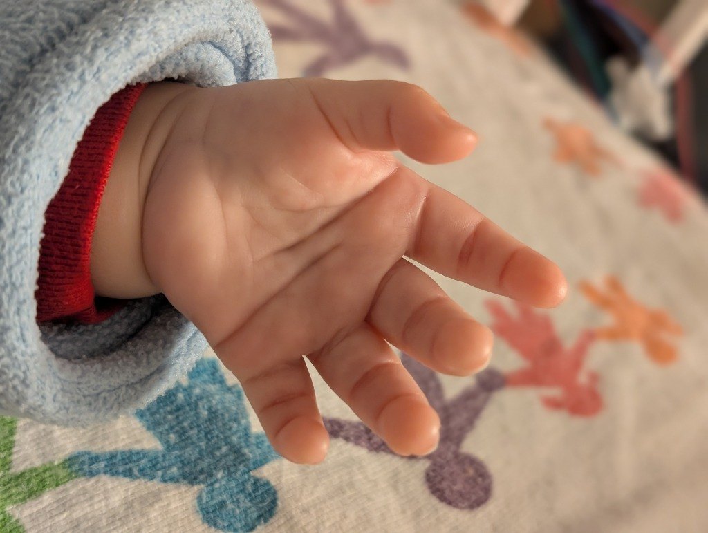 Close-up of Jojo's open hand in a blue fleece sleeve over a colorful blanket